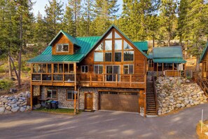 Une cabane en rondins à deux étages, avec un toit en métal vert, des fondations en pierre et un garage.