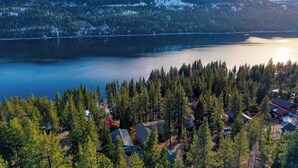 Un conjunto de cabañas junto al lago, rodeado de un denso bosque, una extensa masa de agua y montañas nevadas al fondo.