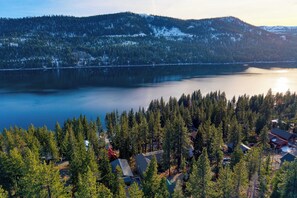 Un ensemble de chalets au bord d’un lac, composé de plusieurs bâtiments entourés d’une forêt dense, avec un vaste plan d’eau et, au loin, des montagnes aux sommets enneigés.