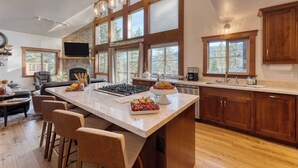 A spacious kitchen with a large island, wooden cabinets, and a stone fireplace. - Denton by Avantstay Hot Tub, Deck w/ Fire Pit Near Skiing & Lake! (Truckee)