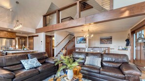 A spacious living room with a large brown leather sofa, a wooden coffee table, and a staircase leading to an upper level. - Denton by Avantstay Hot Tub, Deck w/ Fire Pit Near Skiing & Lake! (Truckee)