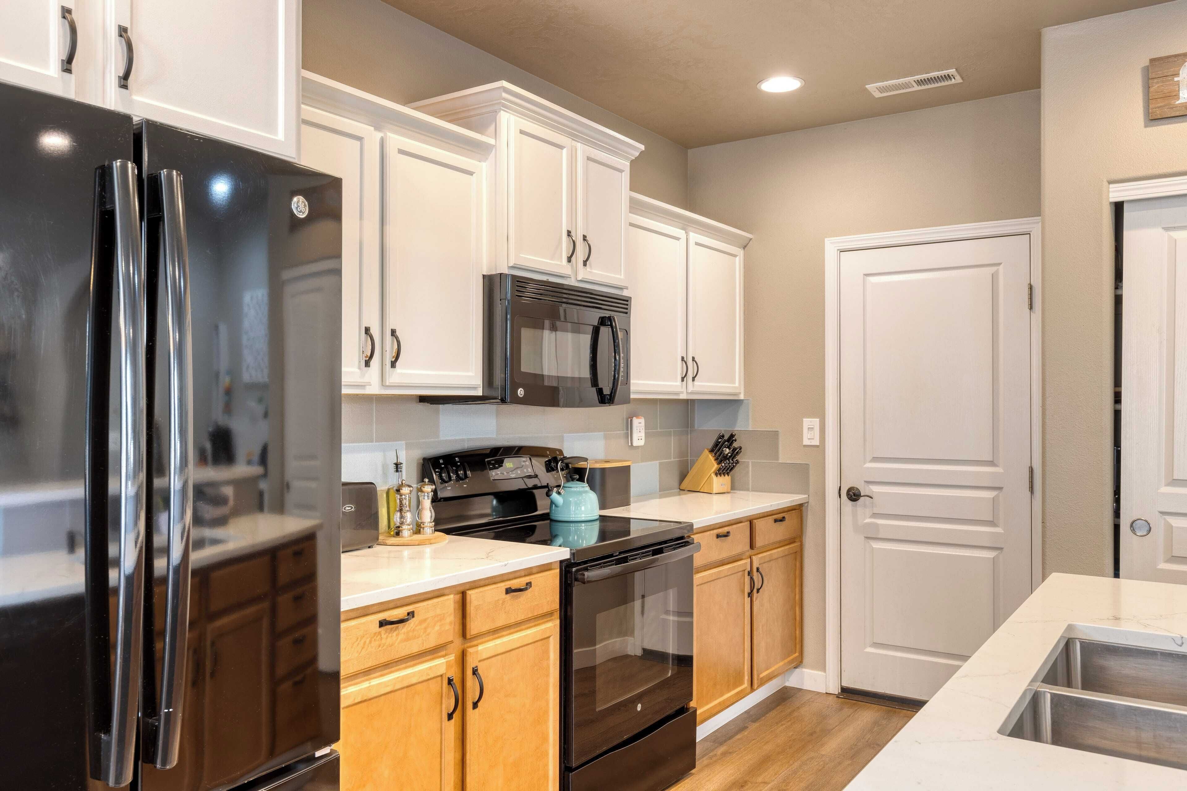 A modern kitchen with white cabinets, a black refrigerator, a microwave, a stove, and a sink.