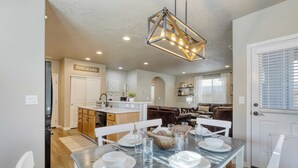 A dining area with a table set for four, a kitchen in the background, and a living area with a couch and coffee table. - Old Mill Getaway by Avantstay Private Backyard w/ Hot Tub (Bend)