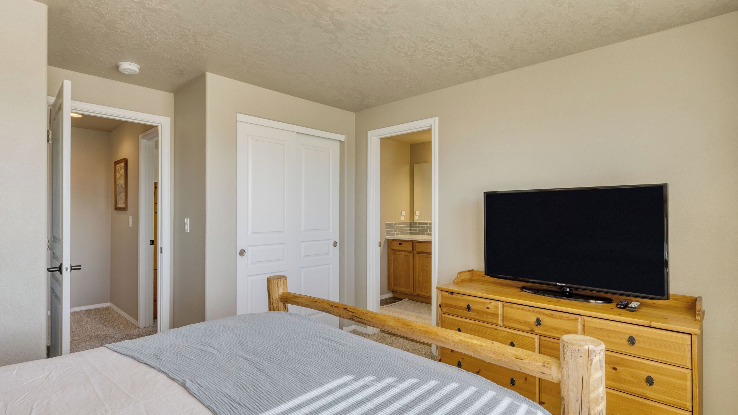 Ein Schlafzimmer mit einem Bett, einem Fernseher auf einer Holzkommode und einer Tür zu einem Badezimmer.