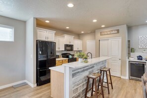 A modern kitchen with white cabinets, a black refrigerator, a microwave, and a built-in island with stools. - Old Mill Getaway by Avantstay Private Backyard w/ Hot Tub (Bend)