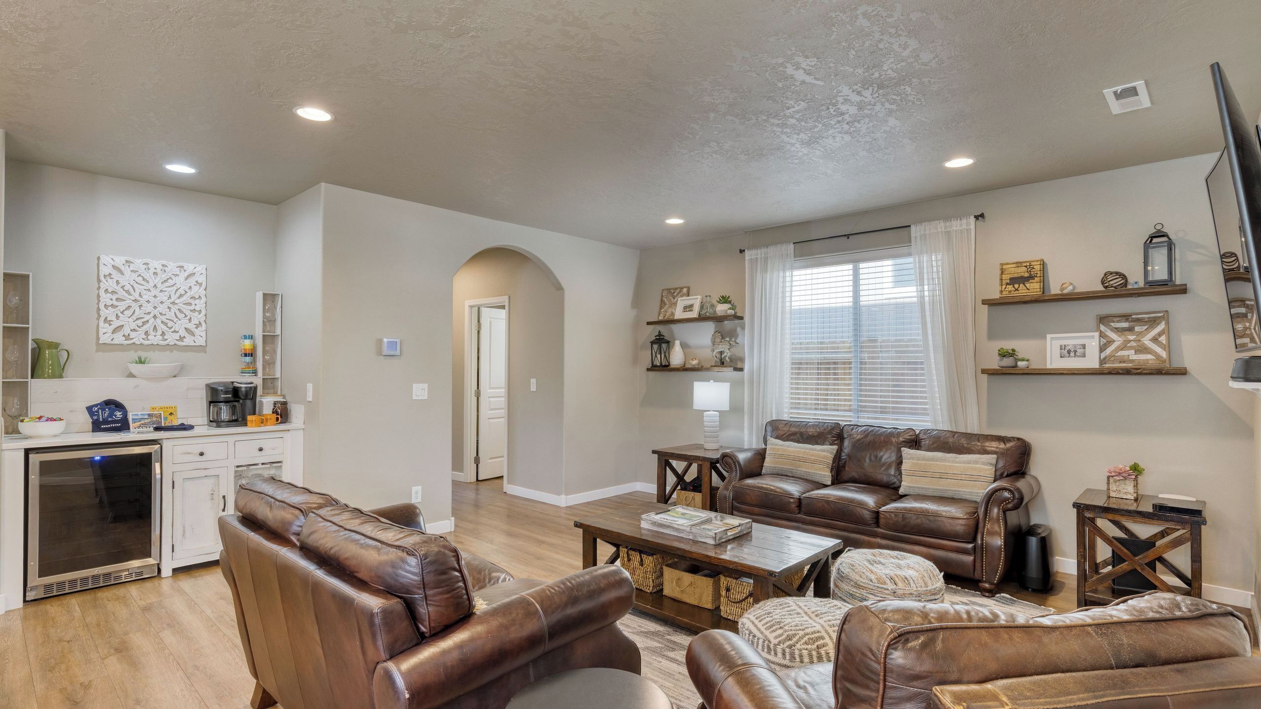 A spacious living room with leather sofas, a coffee table, and a kitchen area with a refrigerator and coffee maker.