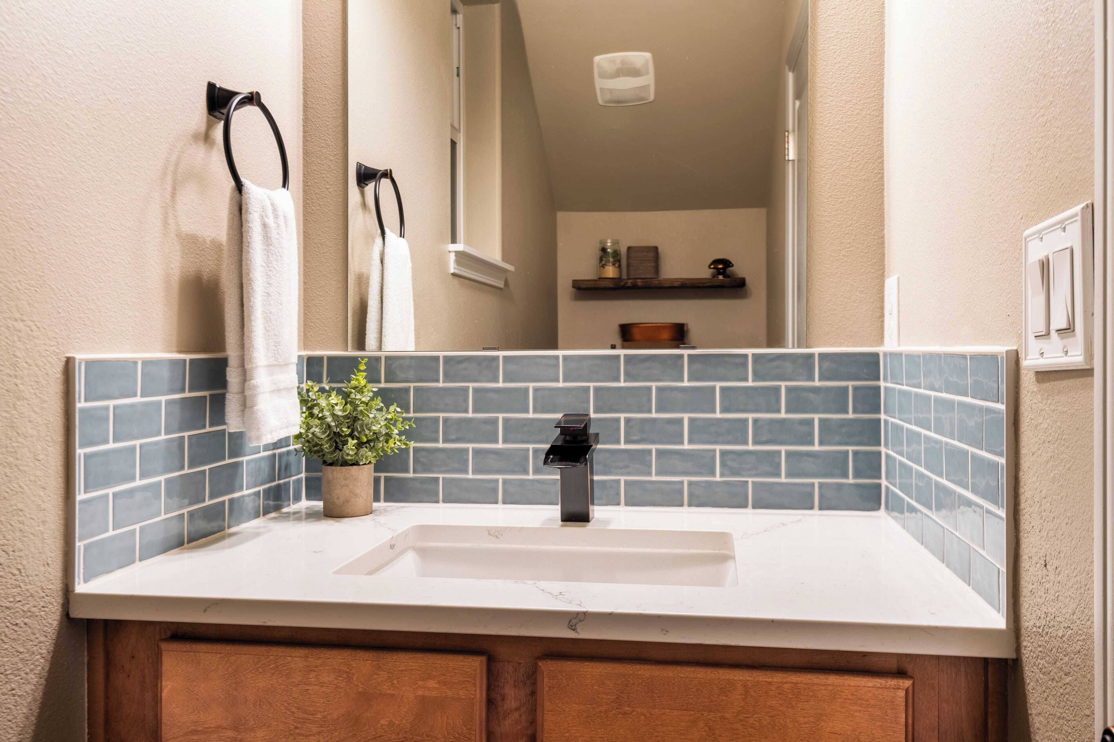 A bathroom with a white sink, blue-tiled backsplash, wooden cabinets, and a potted plant.