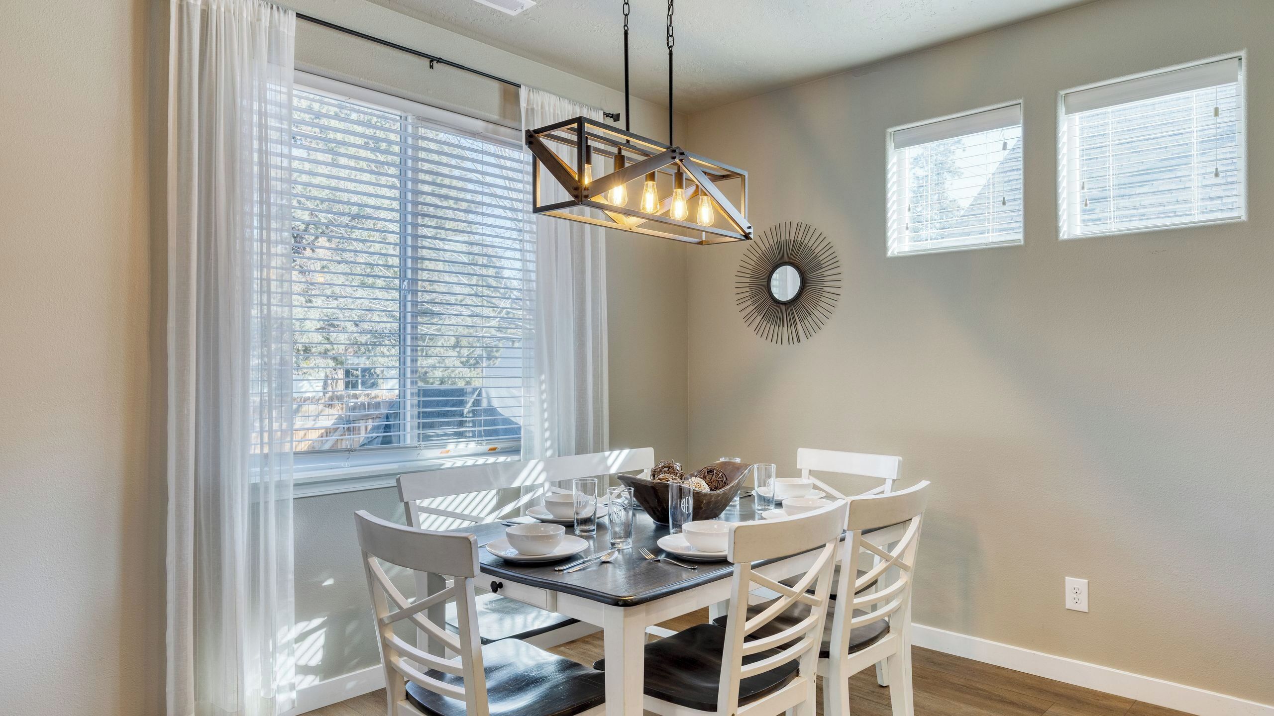 A dining area with a table set for four, a pendant light, and a wall-mounted mirror.