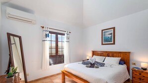 Une chambre à coucher avec un lit en bois, une table de chevet, une commode, un miroir, une fenêtre avec des rideaux et un tableau accroché au mur.