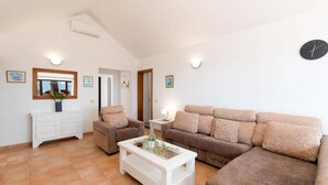 Un salon avec un canapé, un fauteuil et une table basse. On y trouve également un meuble blanc, un miroir et une horloge au mur.