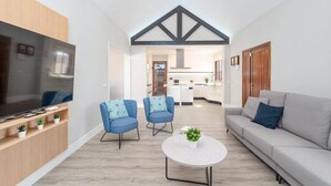 A modern living room with a TV, two blue armchairs, a grey sofa, and a round coffee table.