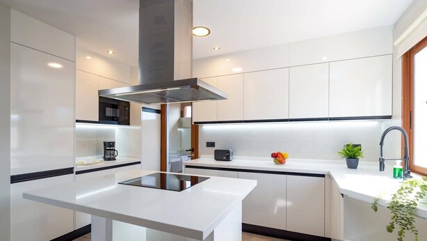 A modern kitchen with white cabinetry, a central island, and a stainless steel range hood.