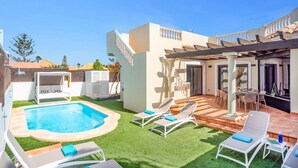 A backyard with a swimming pool, sun loungers, a pergola, and a patio area.