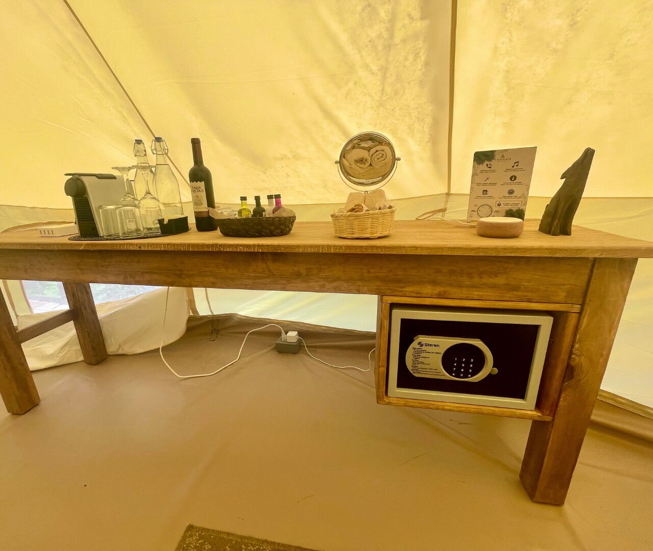 A wooden table with a built-in safe, a mirror, and various bottles and glasses.