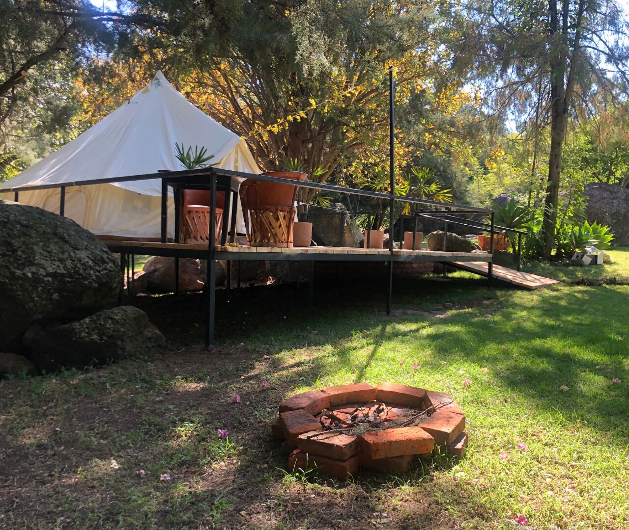Una carpa montada en un área cubierta de césped, con un hoyo para el fuego cerca.