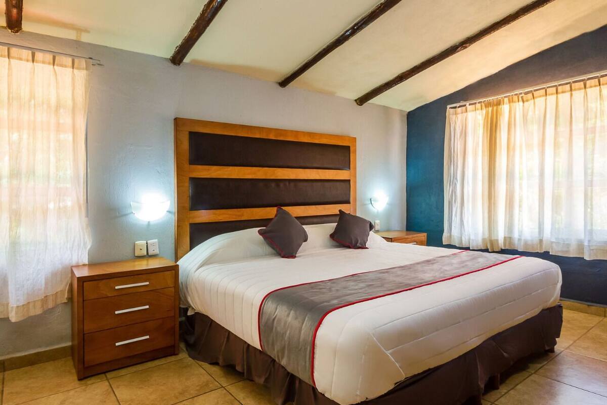 A bedroom with a large bed, wooden headboard, bedside tables, and curtains.