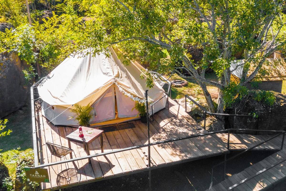 A tented accommodation with a wooden deck, a table, chairs, and a railing.