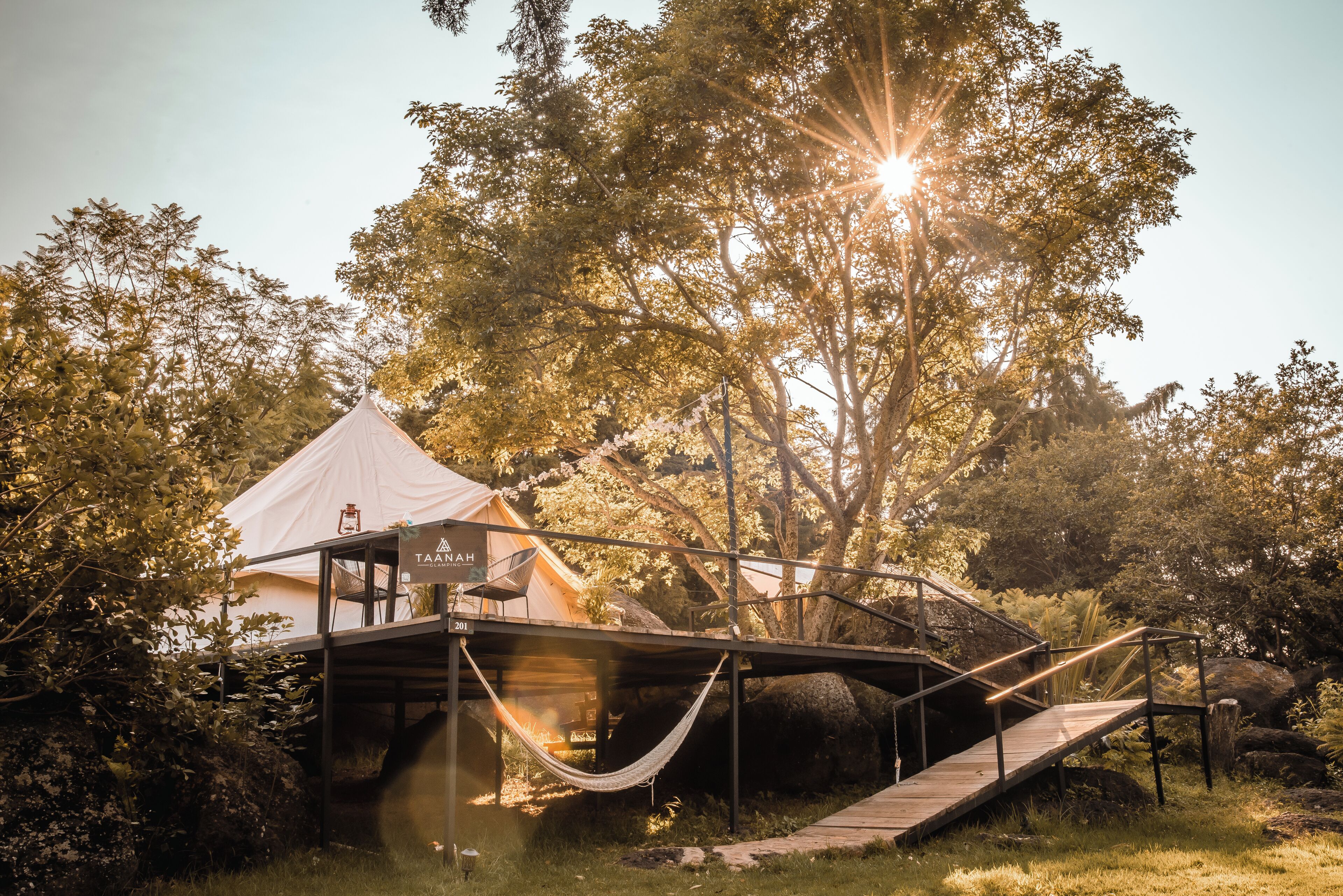 A tented accommodation with a wooden deck and hammock, surrounded by trees and rocks.
