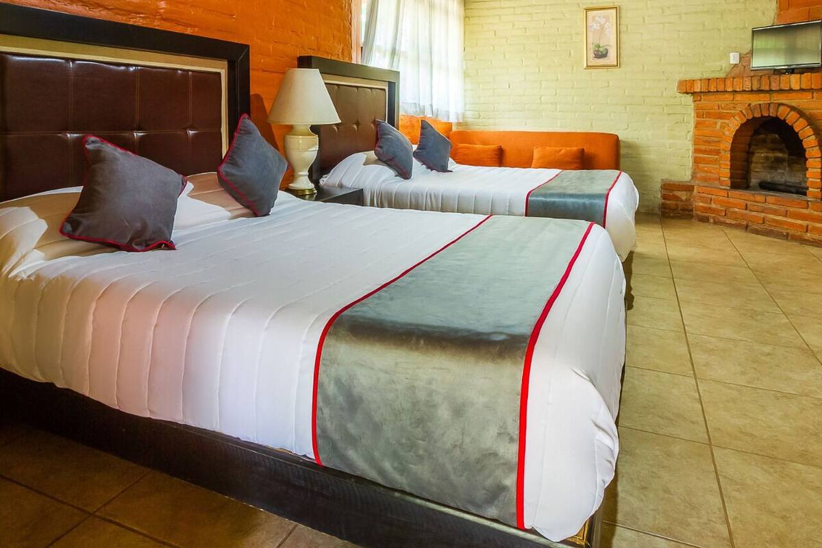 A hotel room with two beds, a brick fireplace, and a wooden ceiling.