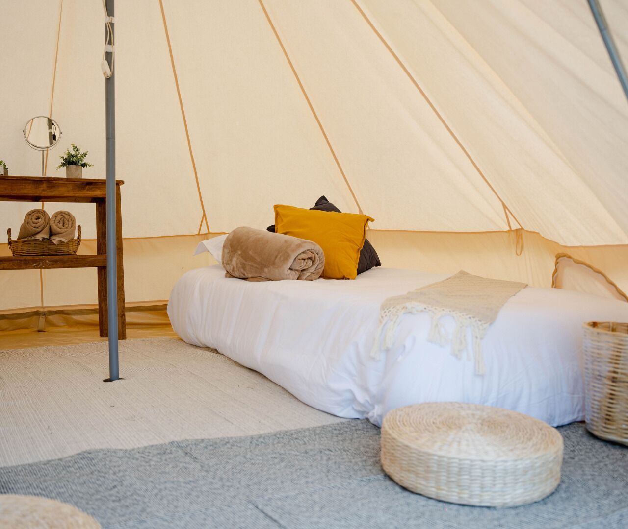 Een tent met een bed, een klein tafeltje met handdoeken en een gevlochten mand.