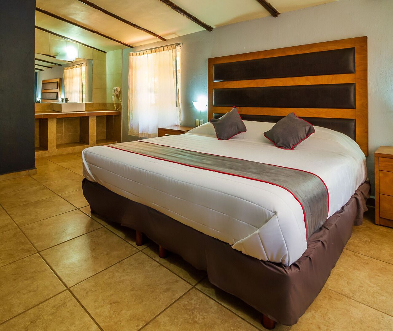 A spacious bedroom with a large bed, a wooden headboard, and a bathroom visible in the background.