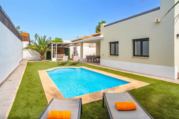 A swimming pool with two lounge chairs and a patio area with a table and chairs.