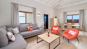 Una sala de estar moderna con un sofá gris, dos sillones rojos, una mesa de centro de madera y un comedor con una mesa y sillas.