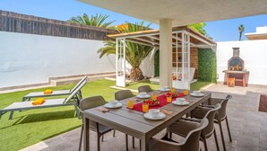 Un patio al aire libre con una mesa de comedor lista para cuatro personas, rodeado de sillas de mimbre.