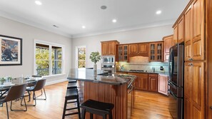 A modern kitchen with wooden cabinets, stainless steel appliances, and a large island with bar stools. - Sunset Pointe by Avantstay Waterfront, Beach, Fire Pit Sleeps 14 5bdr 4BA (Troutman)