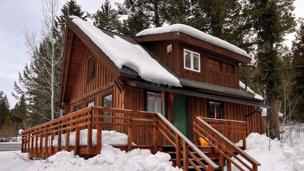 A wooden cabin with a snow-covered roof and a wooden staircase leading to the entrance. - Cozy Woodland Escape: Scenic Cabin Retreat in Alpine, WY (Alpine)