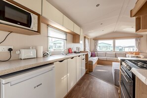 A compact kitchen with a Bosch refrigerator, microwave, and stove, a sink, and a window overlooking a residential area.