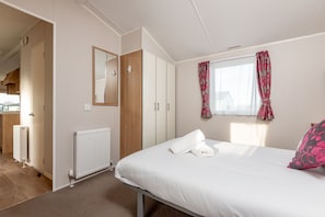 A bedroom with a bed, a radiator, a wardrobe, and a window with curtains.