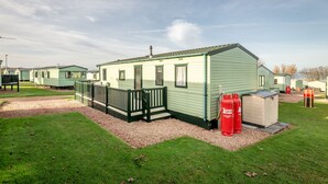 A single-story mobile home with a fenced porch, a small attached shed, and two red gas cylinders.