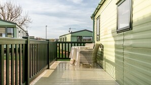 A covered outdoor area with a wooden deck, a wicker chair, and a small table.