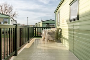 A covered outdoor area with a wooden deck, a wicker chair, and a small table.