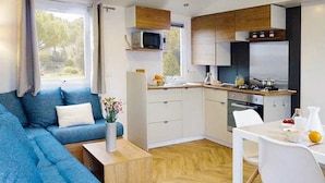 Een knus woongedeelte met een blauwe bank, een eettafeltje en een kitchenette.