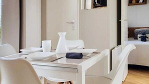 A modern, minimalist room with a white dining table set for two, a small window, and a bed with a headboard. - ZEcamping 4 étoiles 500m plage parc aquatique mobil-home 31m2 (Sainte Brevin-les-Pins)