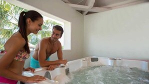 Un couple se tient près d’un jacuzzi, avec vue sur les palmiers à l’extérieur.