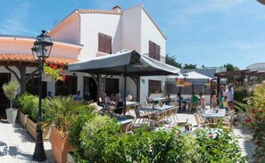 Guests can dine al fresco under the shade of umbrellas, surrounded by lush greenery and the charm of a traditional building.