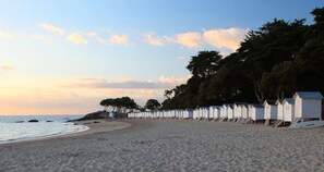 A beach with rows of white beach huts along the shore, a sandy beach, and trees in the background. - ZEcamping 4 étoiles espace aquatique mobil-home 36m2 (Saint-Jean-de-Monts)
