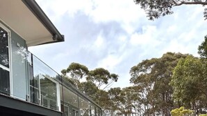 A modern house with a glass facade, stone steps leading to a deck, and a landscaped garden with trees. - The Gem at Depot Beach (Depot Beach)