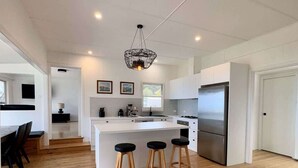 A modern kitchen with a central island, wooden flooring, and a hanging light fixture. - The Gem at Depot Beach (Depot Beach)