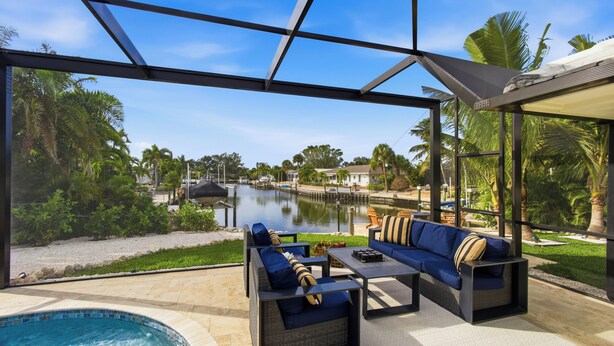 A poolside area with a view of a water body, outdoor furniture, and a glass enclosure.