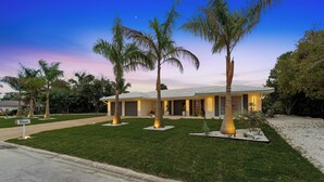 A modern house with a well-maintained lawn, palm trees, and a driveway.