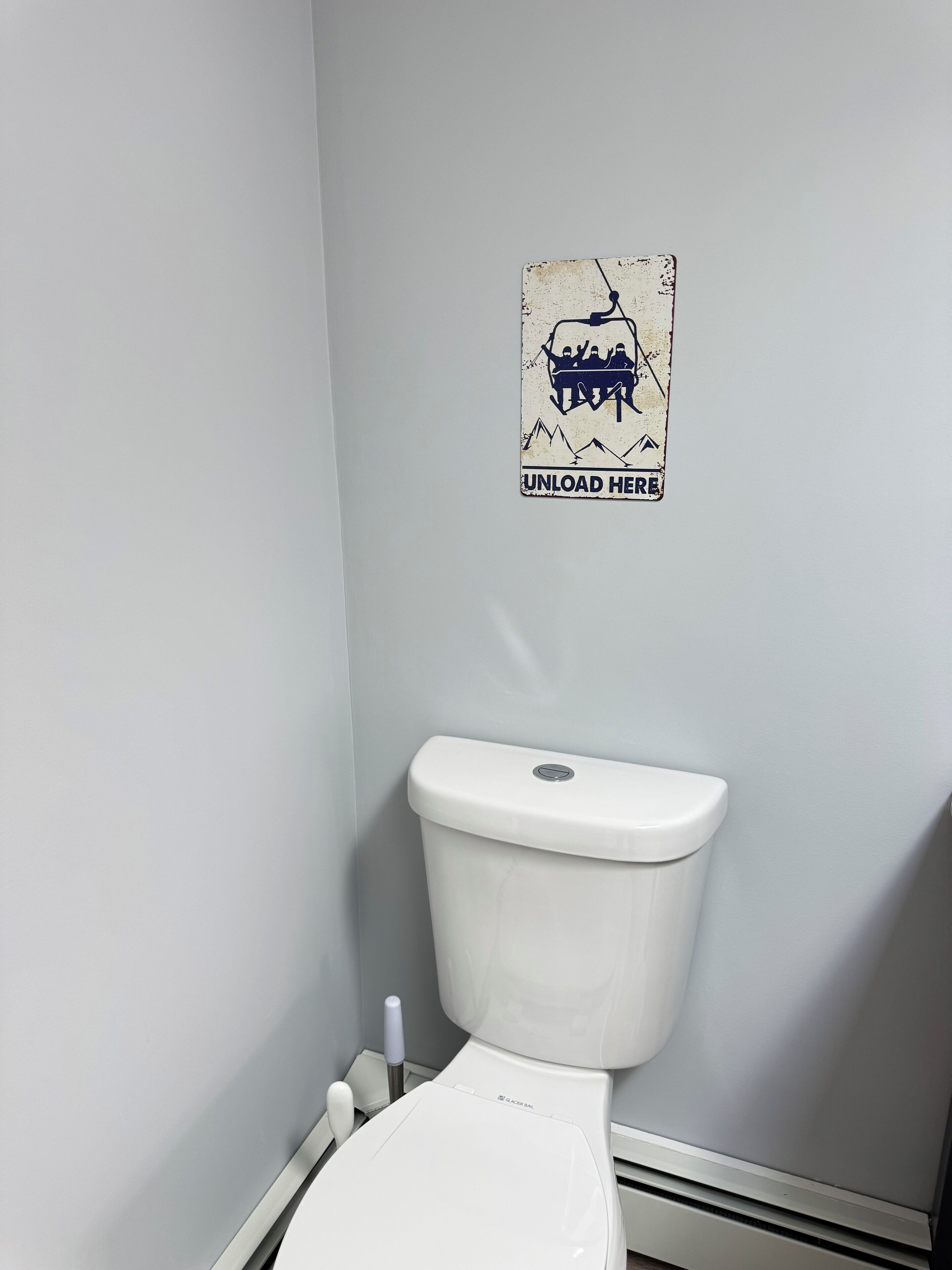 A toilet with a white seat and lid, a wall-mounted sign above it, and a small white object on the floor beside the toilet.