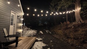 Un banc en bois devant une maison, avec des guirlandes lumineuses suspendues au-dessus.