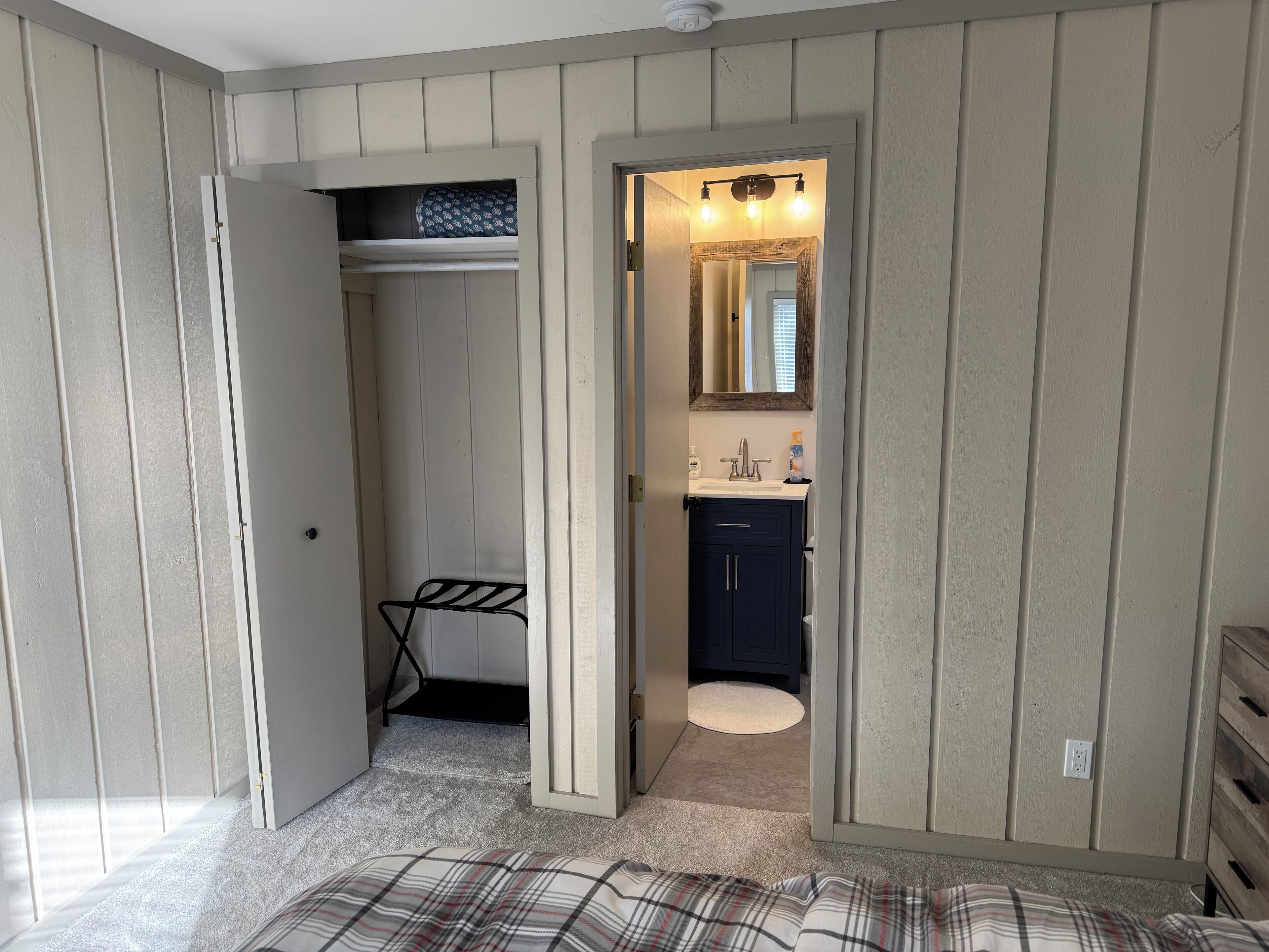 Una habitación con cama, armario y baño con espejo y lavamanos.