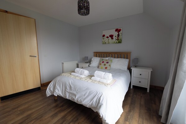 A neatly made bed with white linens and towels, a wooden headboard, and a small bedside table with a lamp.