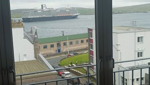 A view of a cruise ship docked at a port with buildings and a road in the foreground. - Lerwick Penthouse Apartment (Lerwick)