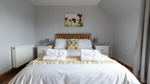 A neatly made bed with white linens and two towels, a wooden headboard, bedside tables with lamps, and a wall-mounted picture of red flowers. - Lerwick Penthouse Apartment (Lerwick)